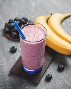 Picture of a blueberry smoothie with a banana and blueberries around the glass for a blueberry smoothie recipe blog.